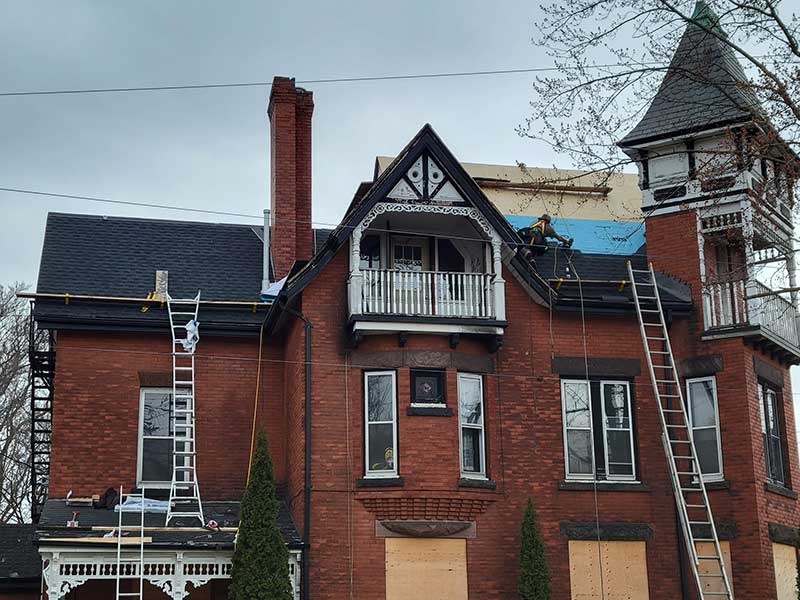 Quality Care Roofing installing new black shingles on a very large, higher-end, three-story red brick home